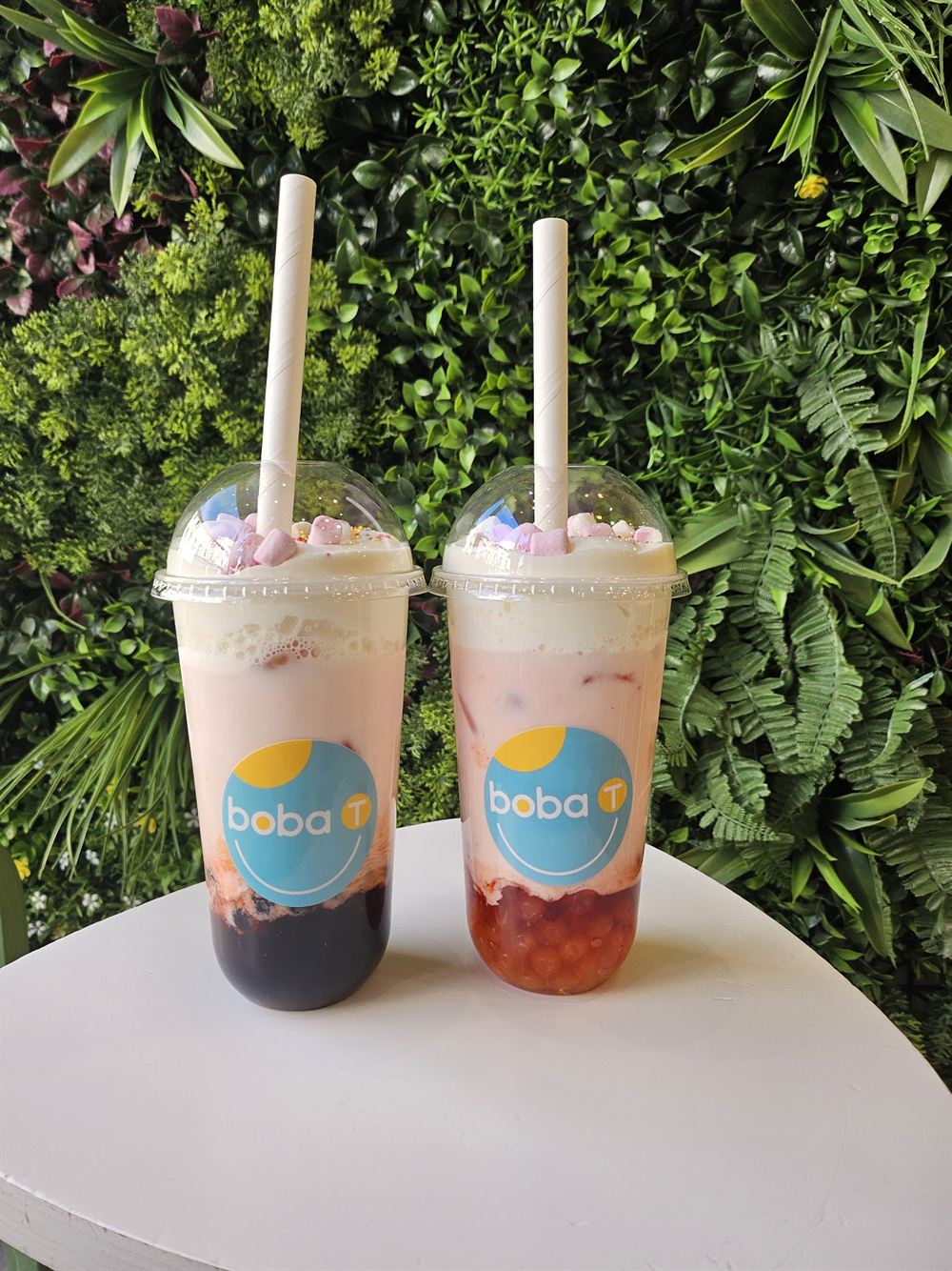 Deux bubble teas roses à la crème, devant un mur végétal